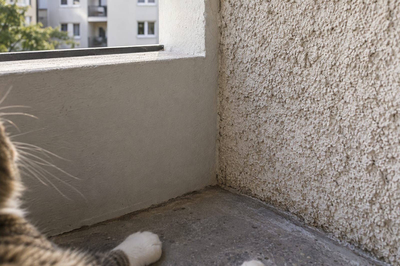 Balkonecke mit glatt gestrichenem Beton links und rauem, sandendem Putz rechts im Streiflicht